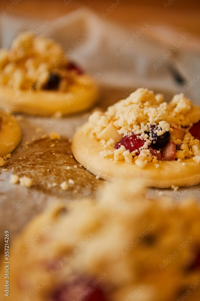 homemade buns with fruit and crumble on white baking paper ready for baking in the oven.