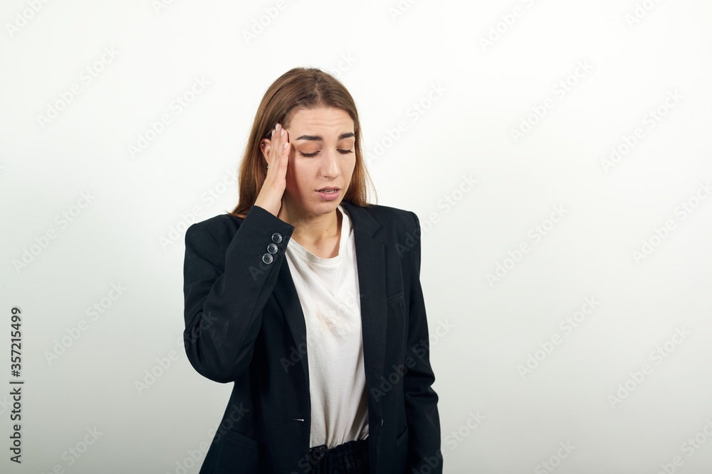 Headache grimacing pain holds the back of neck indicating location. Fatigue during workaholism labor. Young attractive woman with brown hair in a light t-shirt and black jacket on white background Headache grimacing pain holds the back of neck indicating location. Fatigue during workaholism labor. Young attractive woman with brown hair in a light t-shirt and black jacket on white background