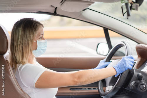 Young blond northern woman driving the car and wearing protective face mask and gloves - Focus on the face mask - Concept of the new normality