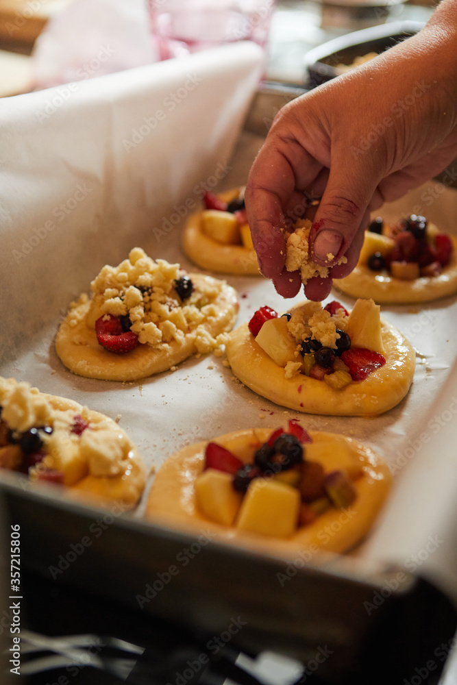 a woman's hand puts crumble on fresh buns with fruit, ready to bake in the oven.
