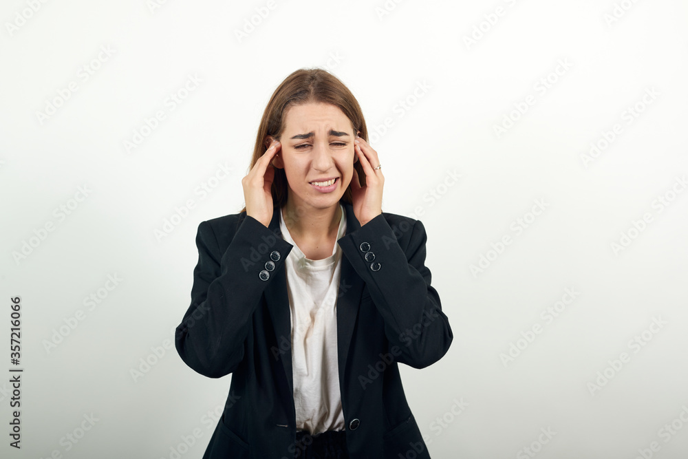 Headache grimacing pain holds the back of neck indicating location. Fatigue during workaholism labor. Young attractive woman with brown hair in a light t-shirt and black jacket on white background Headache grimacing pain holds the back of neck indicating location. Fatigue during workaholism labor. Young attractive woman with brown hair in a light t-shirt and black jacket on white background