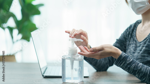 Woman worker wear protective face mask cleaning her hands with sanitizer liquid antibacterial gel, working from home in quarantine, corona virus concept.