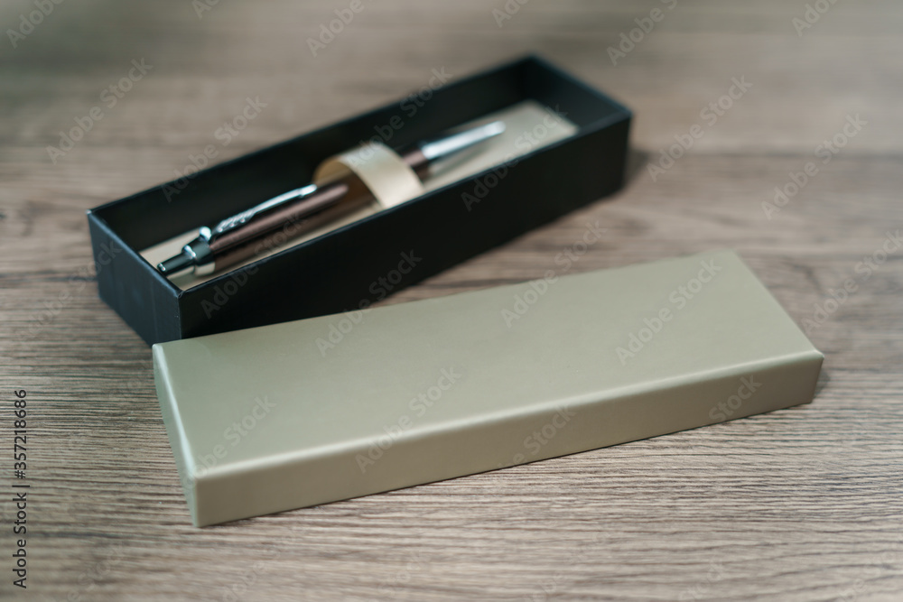 A pen in a gift box on brown wood table background.