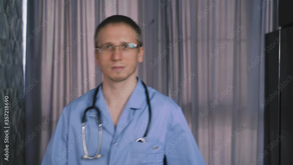 cheerful young doctor wearing blue uniform and glasses with stethoscope takes off and throws away bored protective mask near window curtain at clinic cheerful young doctor wearing blue uniform and glasses with stethoscope takes off and throws away bored protective mask near window curtain at clinic