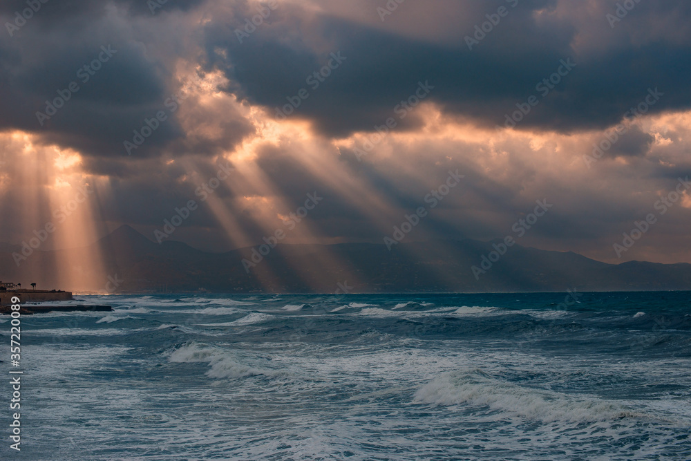 Naklejka premium sunset over the sea with rays of light between storm clouds