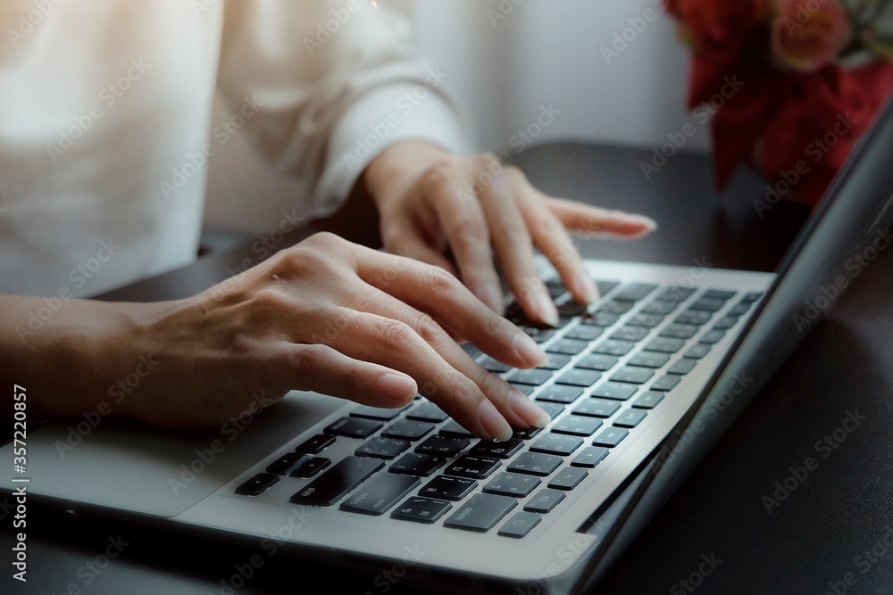 Hands of Asian woman typing report, presentation or operations of internet banking on keyboard of laptop on black desk with red flowers Hands of Asian woman typing report, presentation or operations of internet banking on keyboard of laptop on black desk with red flowers
