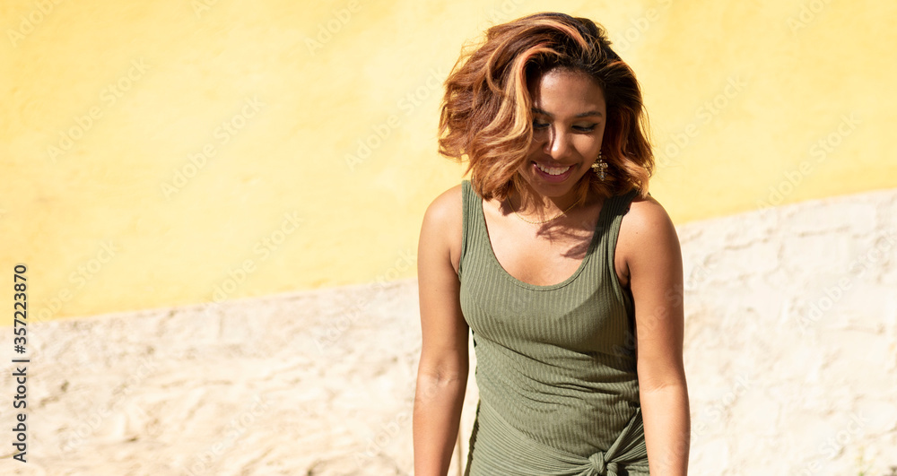 Atractiva mujer joven latina, de piel oscura bronceada, sonriendo en la calle. Lifestyle. Divirtiéndose, con el cabello teñido y peinado usando un vestido verde ajustado Atractiva mujer joven latina, de piel oscura bronceada, sonriendo en la calle. Lifestyle. Divirtiéndose, con el cabello teñido y peinado usando un vestido verde ajustado