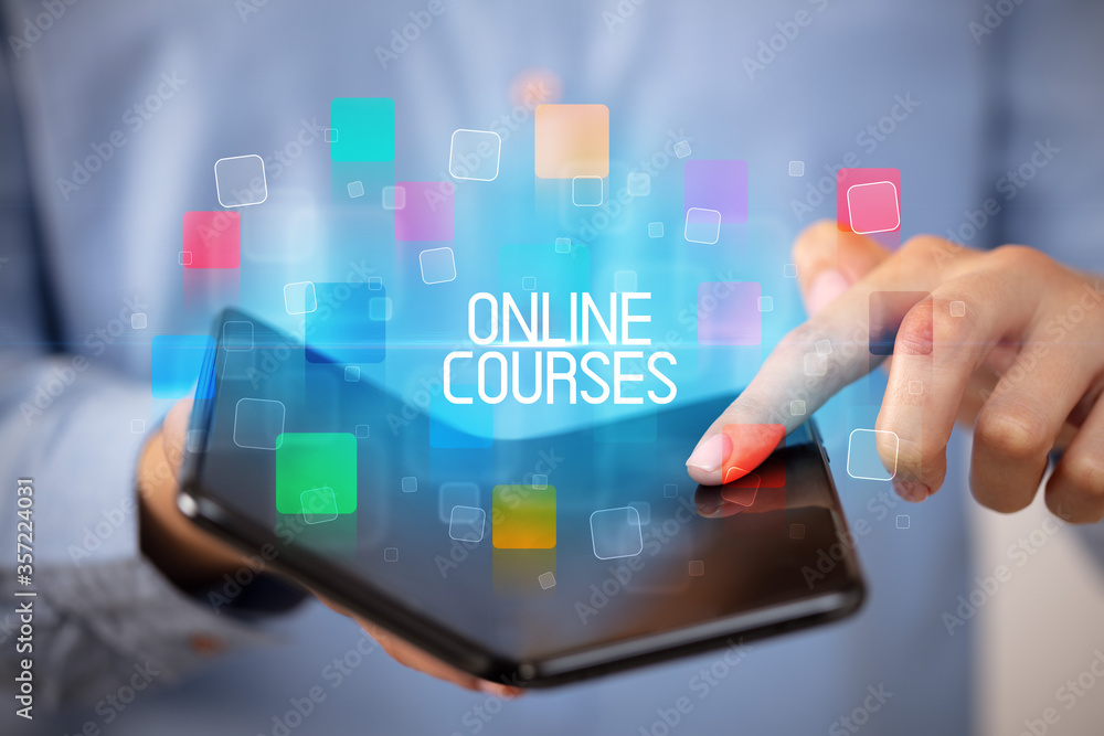 Young man holding a foldable smartphone with ONLINE COURSES inscription, educational concept Young man holding a foldable smartphone with ONLINE COURSES inscription, educational concept