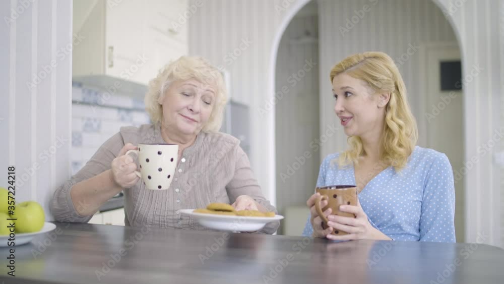 Young woman and mother talking, drinking tea in kitchen, close family relations
