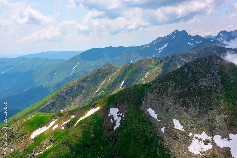 Fototapeta premium stunning landscape in high mountains of romania. grass and spots of snow on the slopes. rocky peak in the distance. clouds on the sky