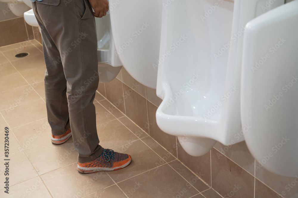 A man standing and urinating in the public man toilet.White ceramic