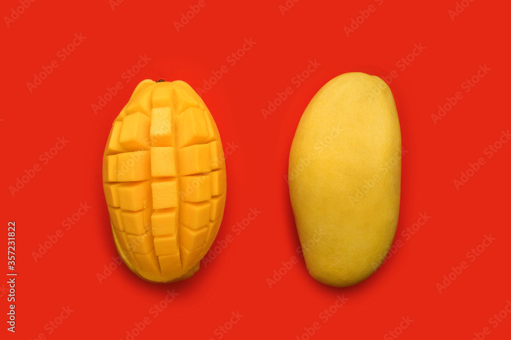 Two 2 yellow mangoes. Fresh tropical ripe fruit, peeled mango, cut into squares or cubes on red background. Top view. How to peel, serve a mango Two 2 yellow mangoes. Fresh tropical ripe fruit, peeled mango, cut into squares or cubes on red background. Top view. How to peel, serve a mango