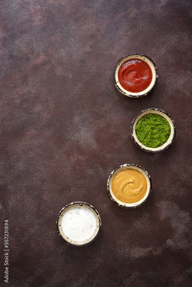 Collection of various sauces in the bowl: tomato, pesto, creamy with greens and mustard on a dark rustic background. Top view, copy space. Collection of various sauces in the bowl: tomato, pesto, creamy with greens and mustard on a dark rustic background. Top view, copy space.