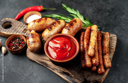 Different grilled sausages with spices and
rosemary, served on a cutting board on a stone background