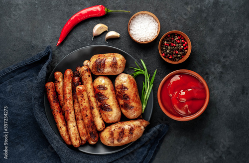 Various grilled sausages with spices on a black plate on a stone background