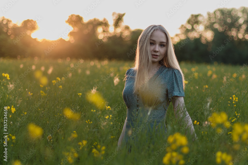 Young happy blonde girl staying at a green wheat field in the evening against the background of the sun shines. Concept of freedom. Summer time joy. Beautiful young woman walking on field. Young happy blonde girl staying at a green wheat field in the evening against the background of the sun shines. Concept of freedom. Summer time joy. Beautiful young woman walking on field.