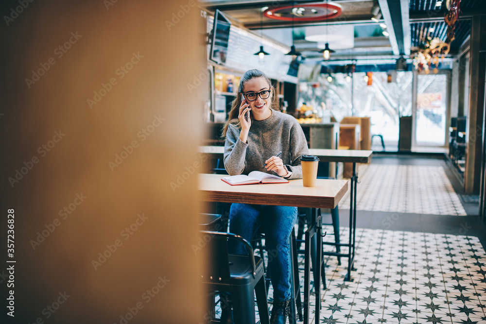 Happy hipster girl sitting at cafeteria table with textbook