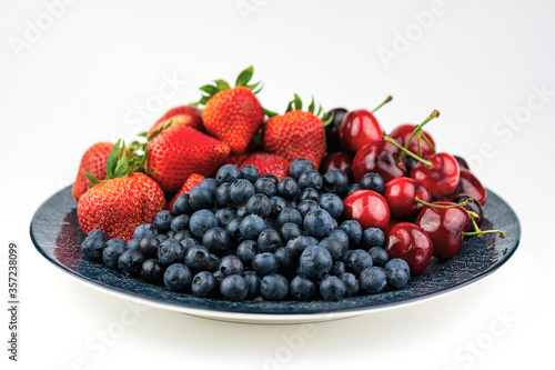 A blue patterned plate with blueberries  strawberries  and cherries on a white background.