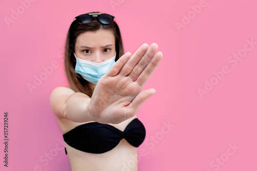 distance, a girl in a swimsuit with an outstretched hand shows the distance between people. girl in a mask and swimsuit. summer on isolation.