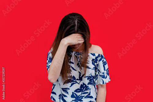 the girl lowered her head and covered her face with her hand. the girl in the one-color isolated background is ashamed.