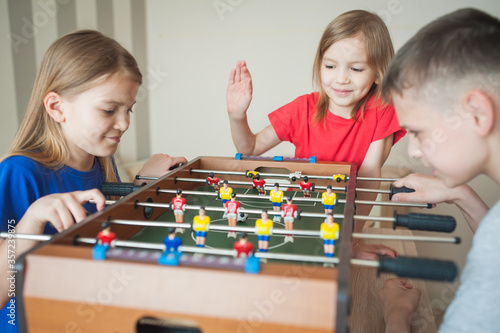 Children play table football in a children's room, two girls and a boy