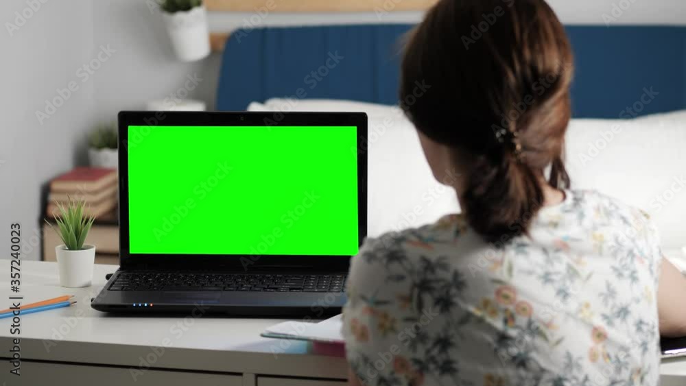 Woman sits at desk in bedroom, she looks at laptop green screen and talks to someone over internet video communications, sometimes taking notes in notebook. Close-up Woman sits at desk in bedroom, she looks at laptop green screen and talks to someone over internet video communications, sometimes taking notes in notebook. Close-up