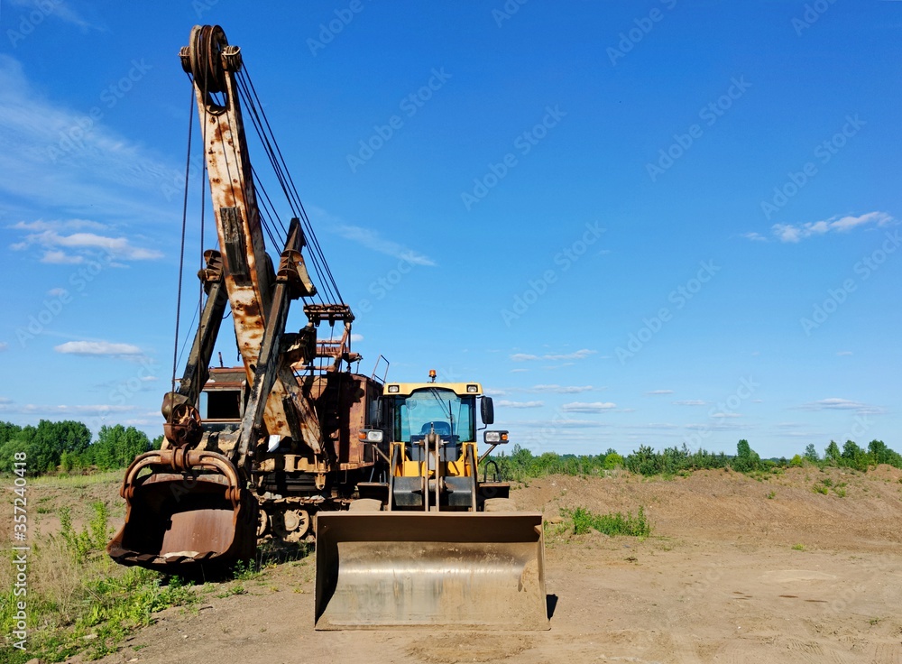 wheel loader and excavator on a site near a sand quarry on a sunny day against a blue sky wheel loader and excavator on a site near a sand quarry on a sunny day against a blue sky