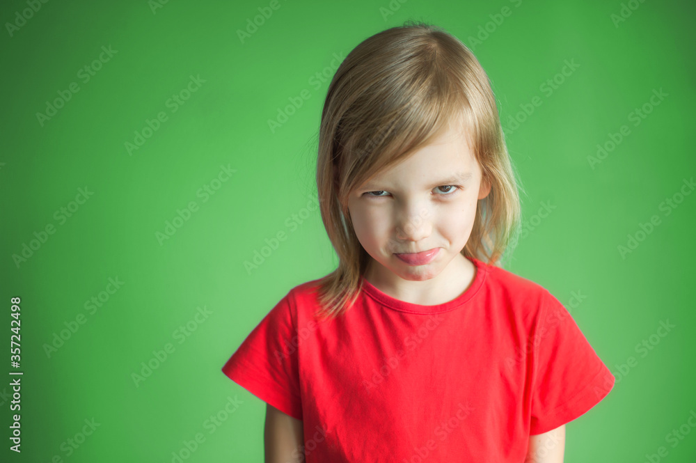 Close-up studio shot of a lovely blond little girl in a red t-shirt and posing against a green background. Offended and looking sullenly Close-up studio shot of a lovely blond little girl in a red t-shirt and posing against a green background. Offended and looking sullenly