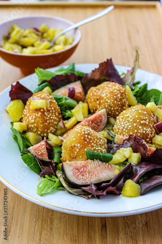 Fancy salad with goat cheese balls, figs and mango over a wooden table. 
