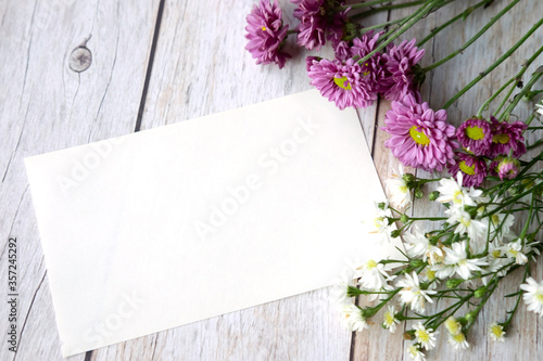 Blank note paper with purple chrysanthemum and white cutter flowers on white wooden table.Top view and copy space for text.