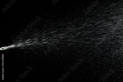 Liquid water spray mist from perfume bottle isolated on black. Aerosol splash background.