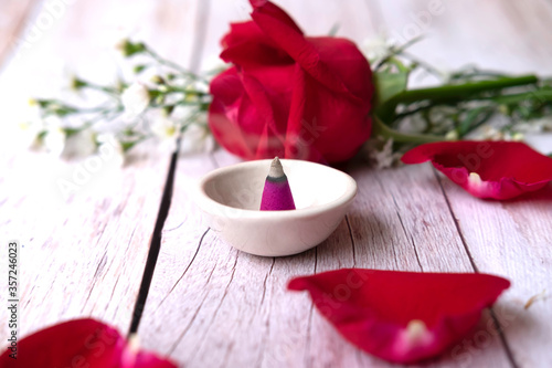 Burning cone incense in small with red rose and white cutter flowers on white wooden table.The comfort of aromatherapy concept.