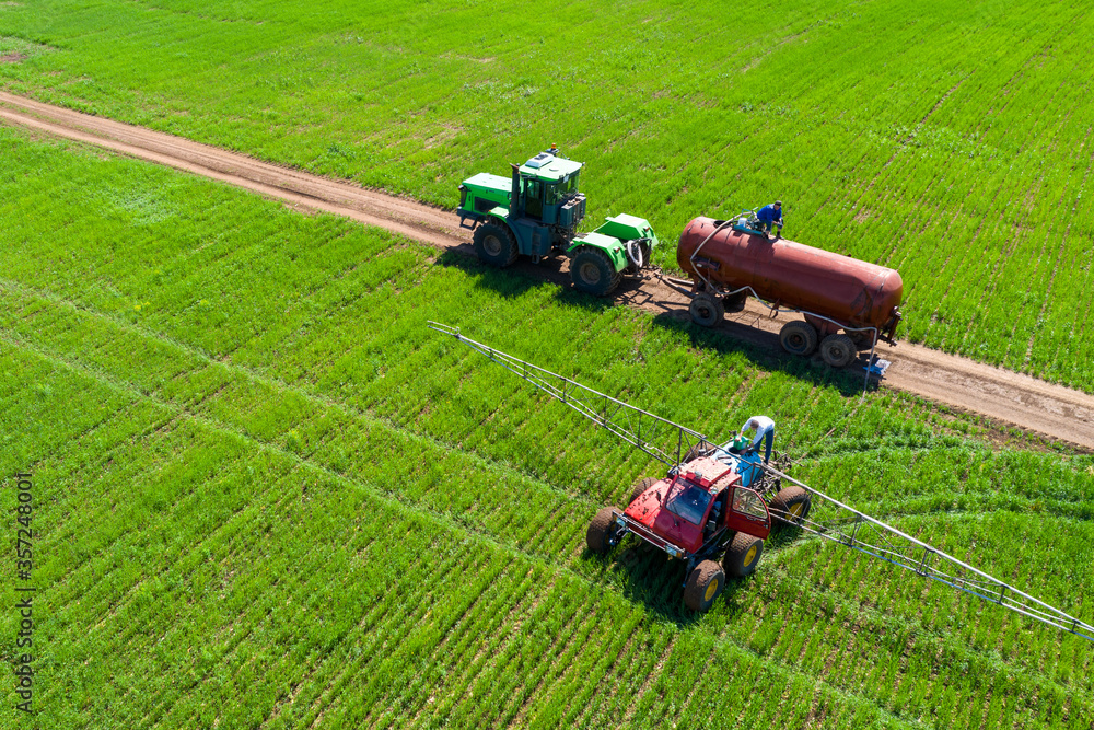 Tractor field treatment with herbicides. The farmer pours a chemical into the sprayer. Next to it is another tractor with a water tank. Shooting from a drone. Tractor field treatment with herbicides. The farmer pours a chemical into the sprayer. Next to it is another tractor with a water tank. Shooting from a drone.