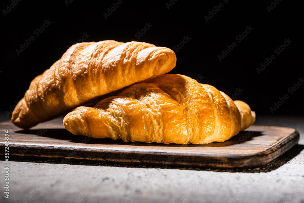 fresh baked croissants on wooden cutting board on concrete grey surface isolated on black