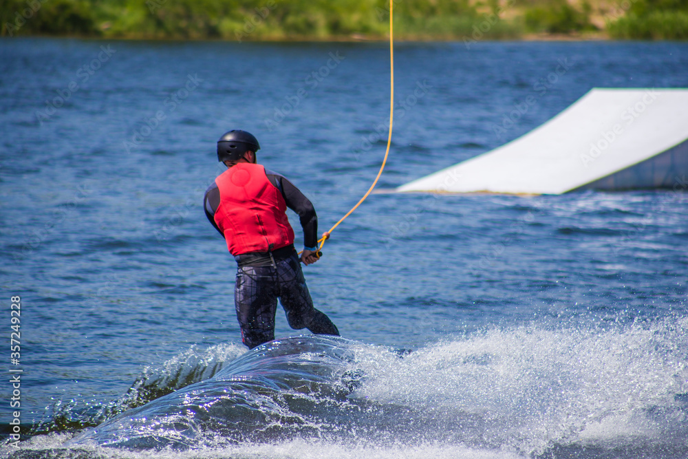 The man does wakeboarding on the water in the summer in a helmet and wetsuit. The man does wakeboarding on the water in the summer in a helmet and wetsuit.