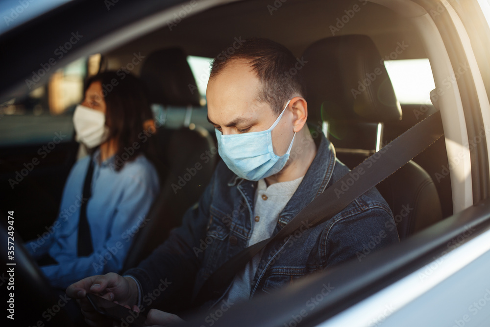 Taxi driver chatting on the mobile cell phone and wearing sterile medical mask while waiting in a traffic during coronavirus pandemic. Social distance, new normal, health concept.