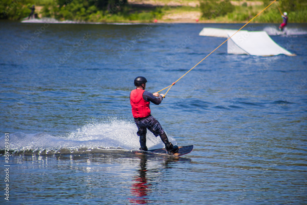 The man does wakeboarding on the water in the summer in a helmet and wetsuit. The man does wakeboarding on the water in the summer in a helmet and wetsuit.