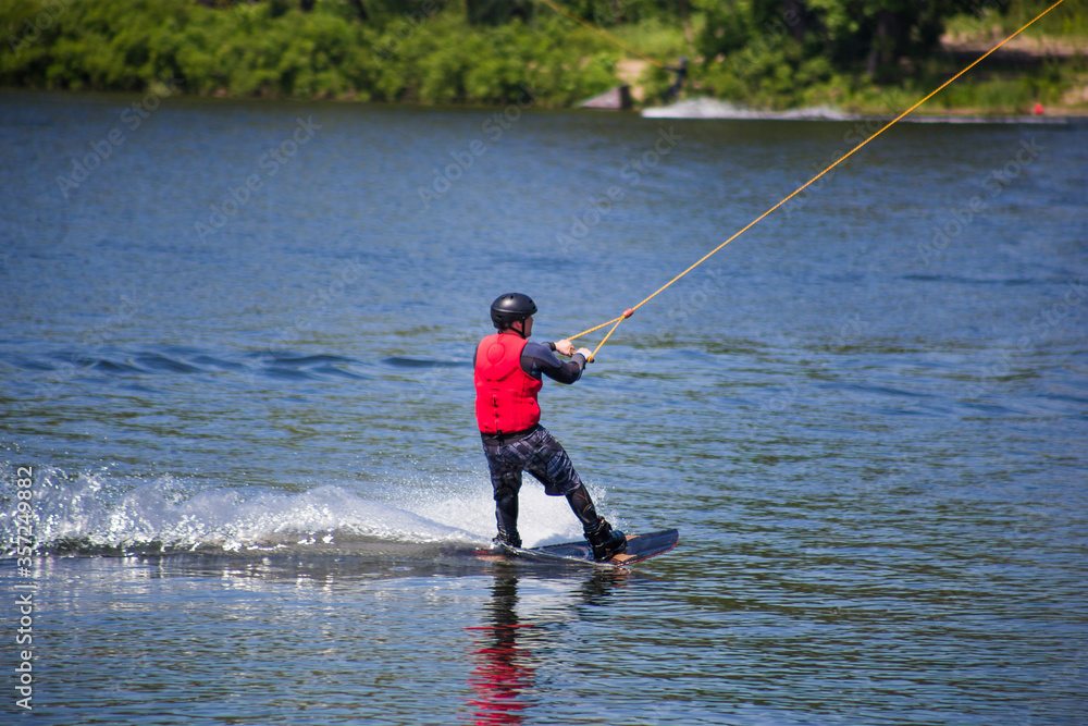 The man does wakeboarding on the water in the summer in a helmet and wetsuit. The man does wakeboarding on the water in the summer in a helmet and wetsuit.