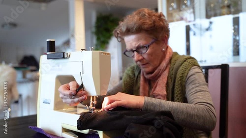 Woman sewing clothes using machine. Elderly woman sews clothes using machine. Mother mends clothes using sewing skills, fabric and thread.
