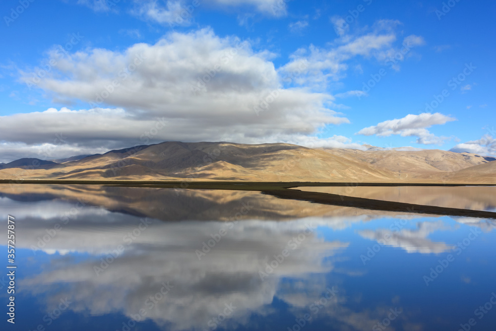Beautiful reflection of hills and clouds in glass like waters of lake in Tibet, Asia