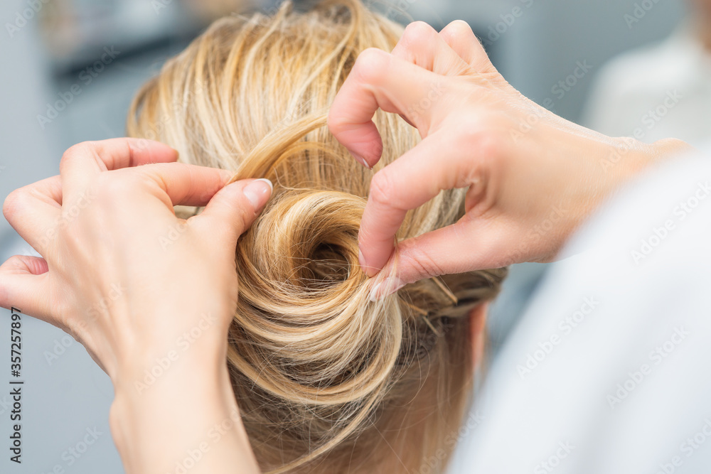 Naklejka premium Close up rear view of hairdresser making hairstyle for long hair of blonde woman.