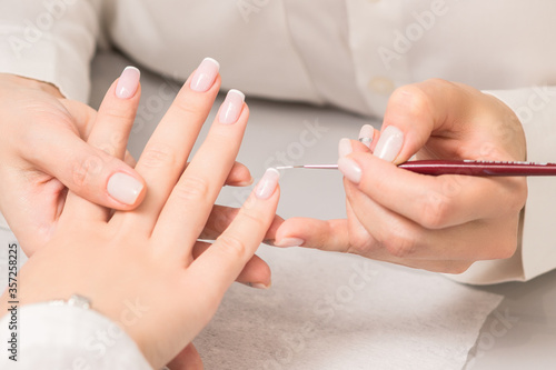 Hand of young woman receiving french manicure by beautician at nail salon.