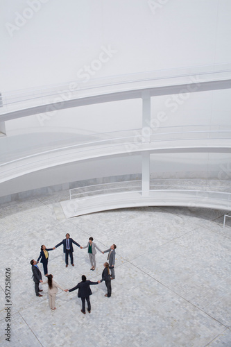 Business people holding hands standing in circle in modern courtyard