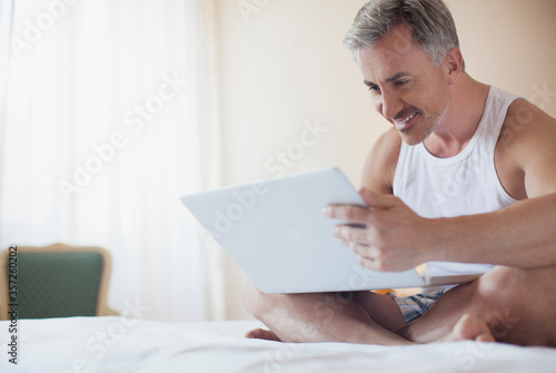 Smiling man using laptop in bed