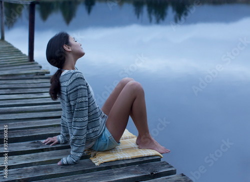 Serene woman sitting on dock over lake