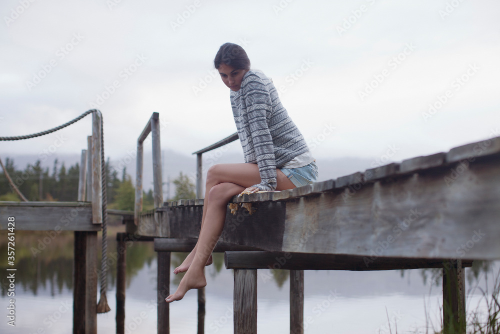 Serene woman sitting at edge of dock over lake