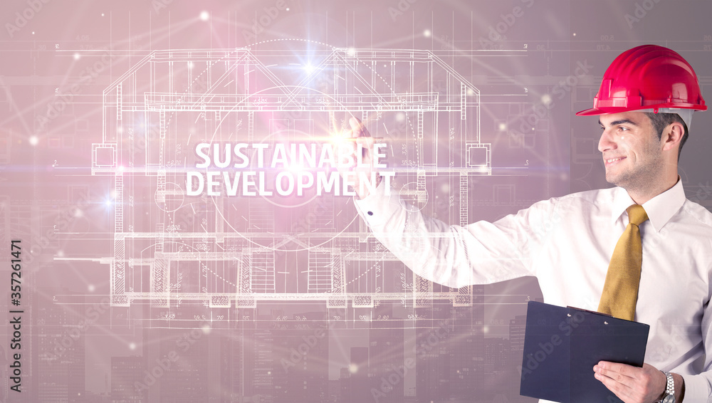 Handsome architect with helmet drawing SUSTAINABLE DEVELOPMENT inscription, new technology concept Handsome architect with helmet drawing SUSTAINABLE DEVELOPMENT inscription, new technology concept