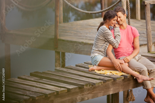 Affectionate couple sitting on dock over lake