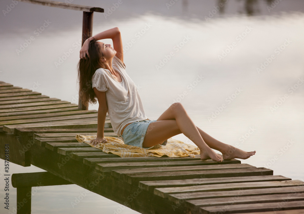 Woman with head back and hand in hair on dock over lake