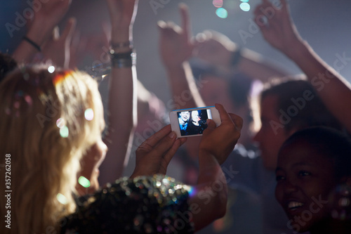 Woman camera phone photographing friends on dance floor of nightclub photo